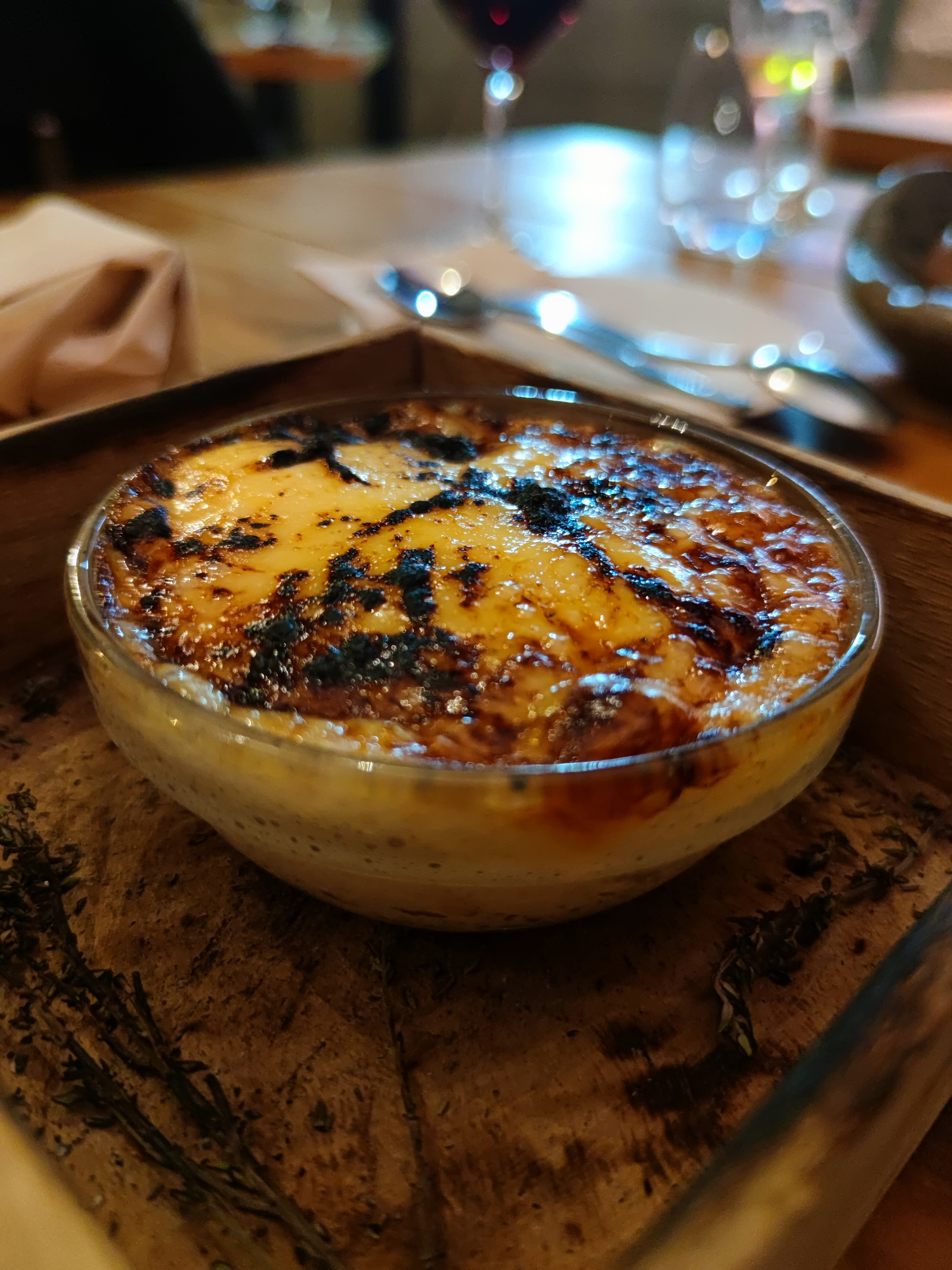 A traditional Portuguese 'Egg Yolk, Citrus and Sugar' dessert served in a clear glass bowl, showcasing layers of creamy light-colored custard with a dark, crackled, caramelized sugar topping.