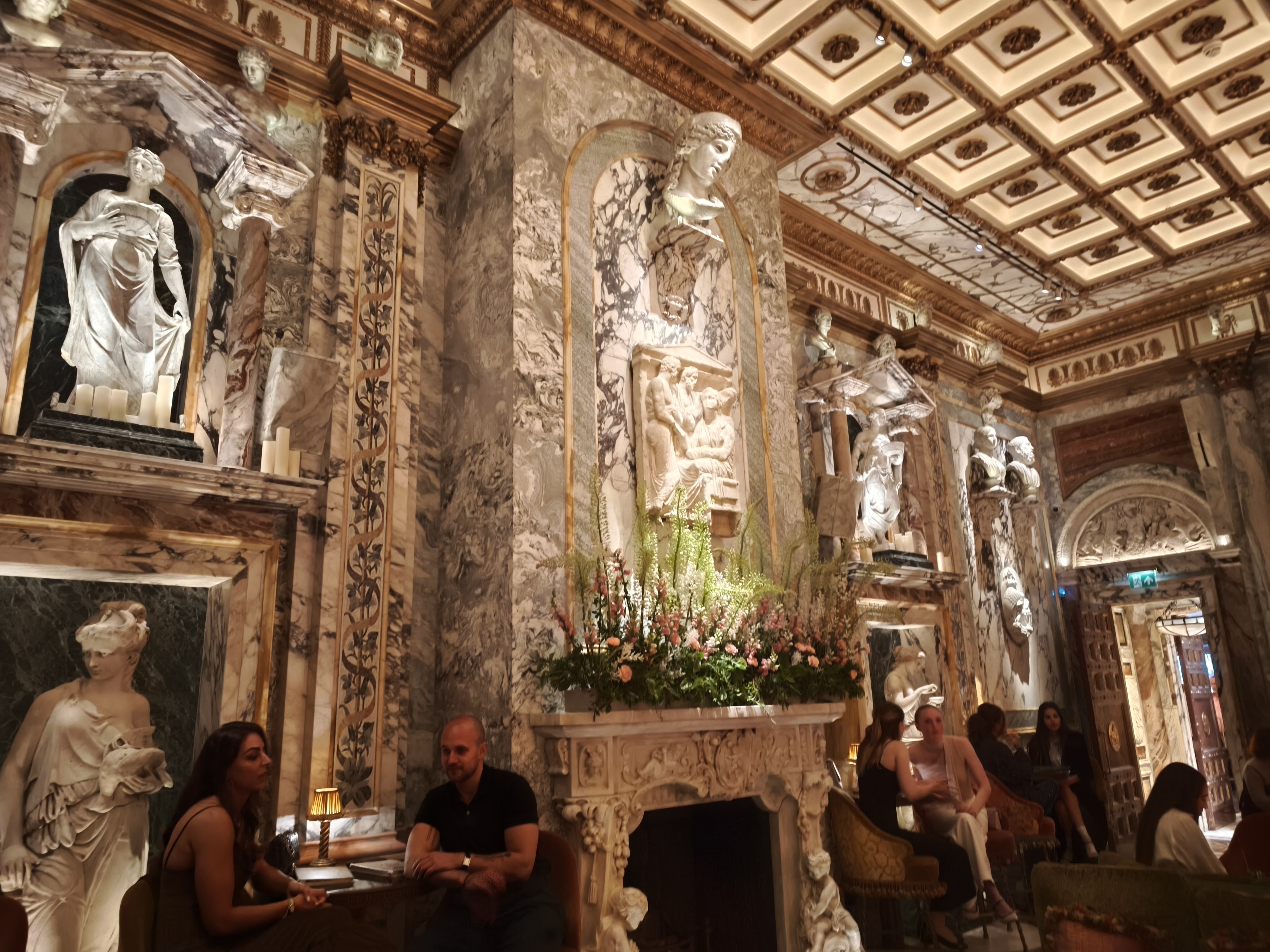The interior of a highly decorated bar with marbled columns, statues in wall niches, and a coffered ceiling.