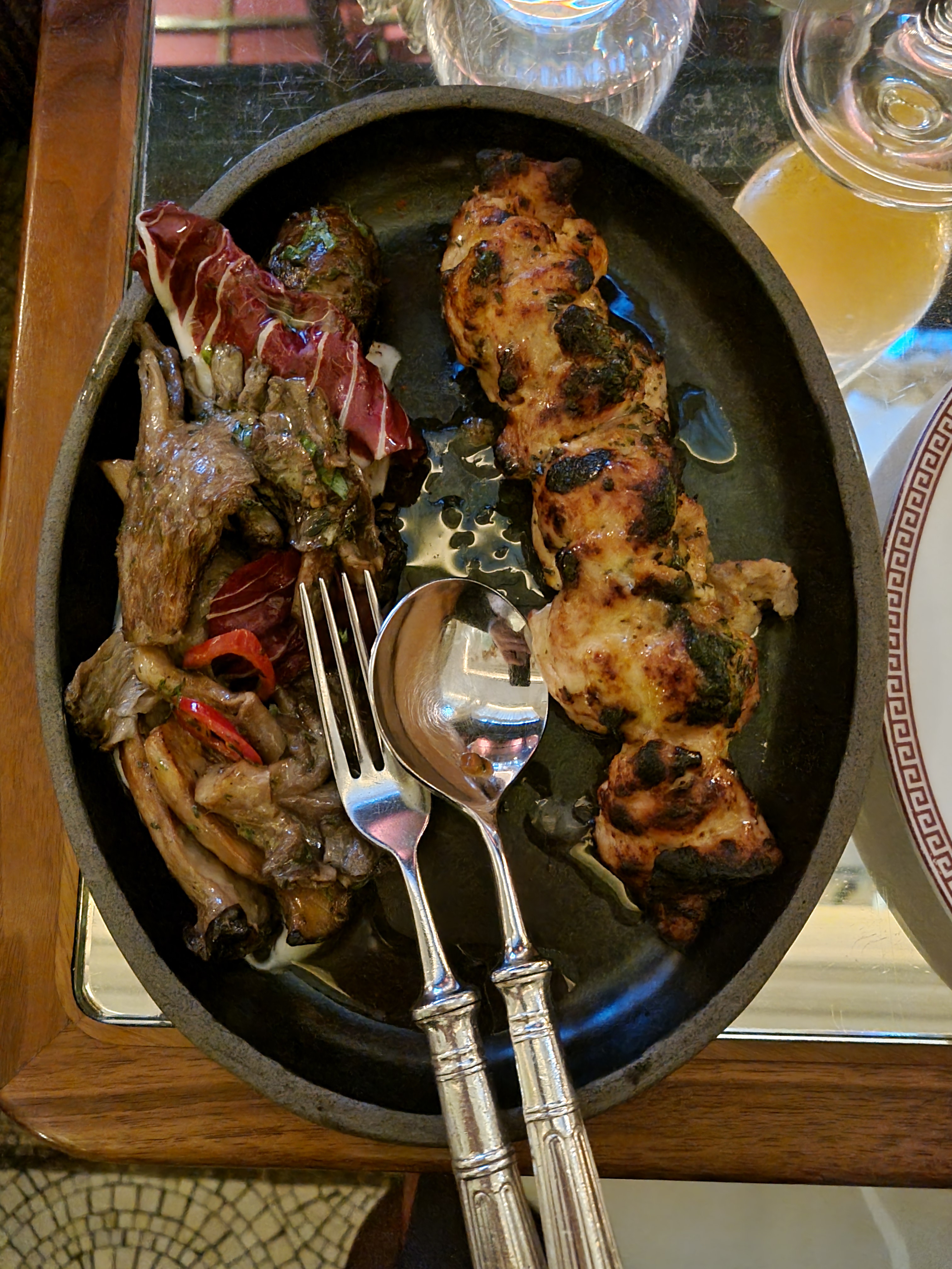 One chicken skewer on a dark, rustic-looking plate. It is served with a side of mushrooms and greens.