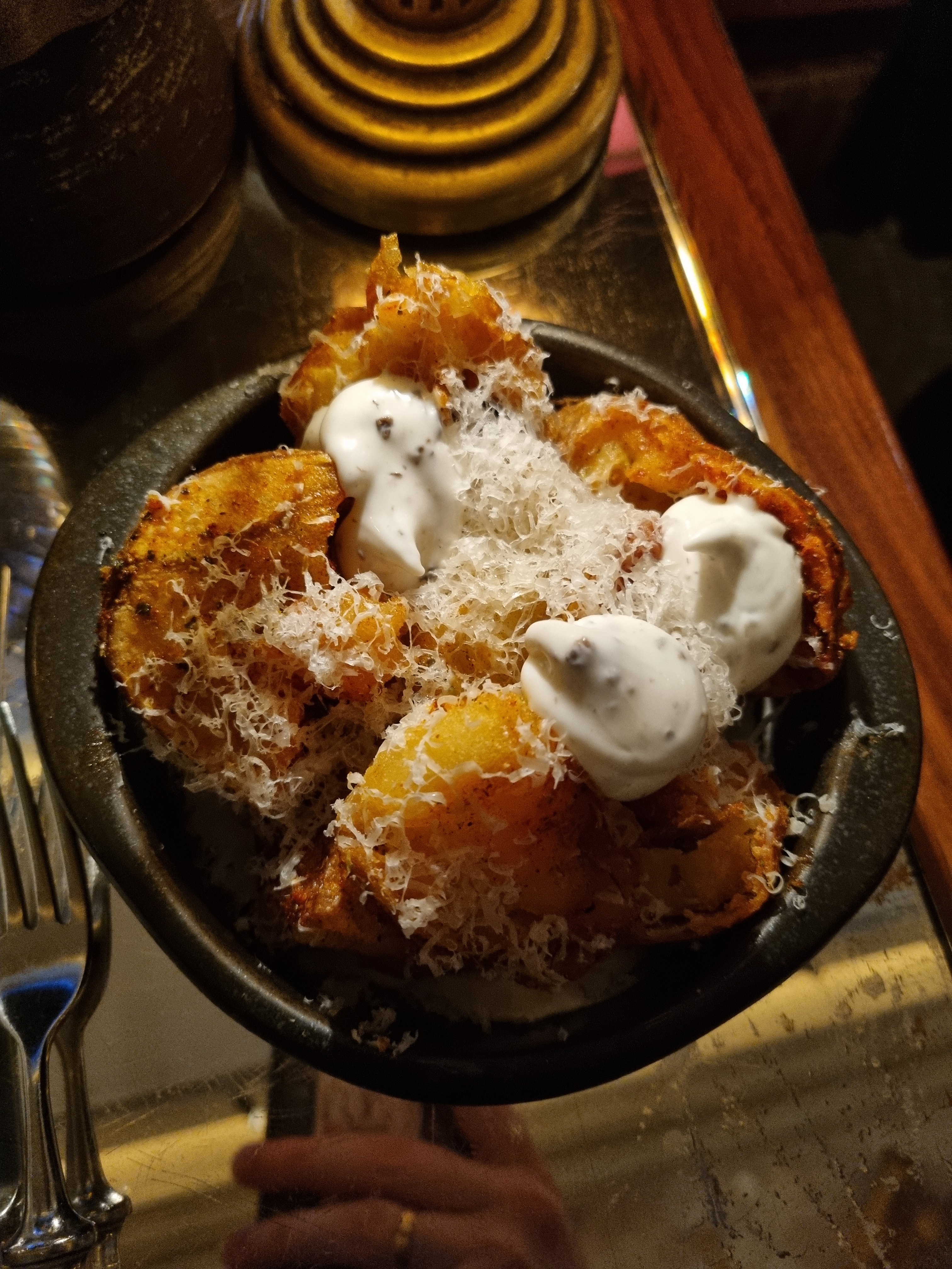 A bowl of golden-brown fried potatoes topped with grated parmesan cheese and three dollops of white sauce.