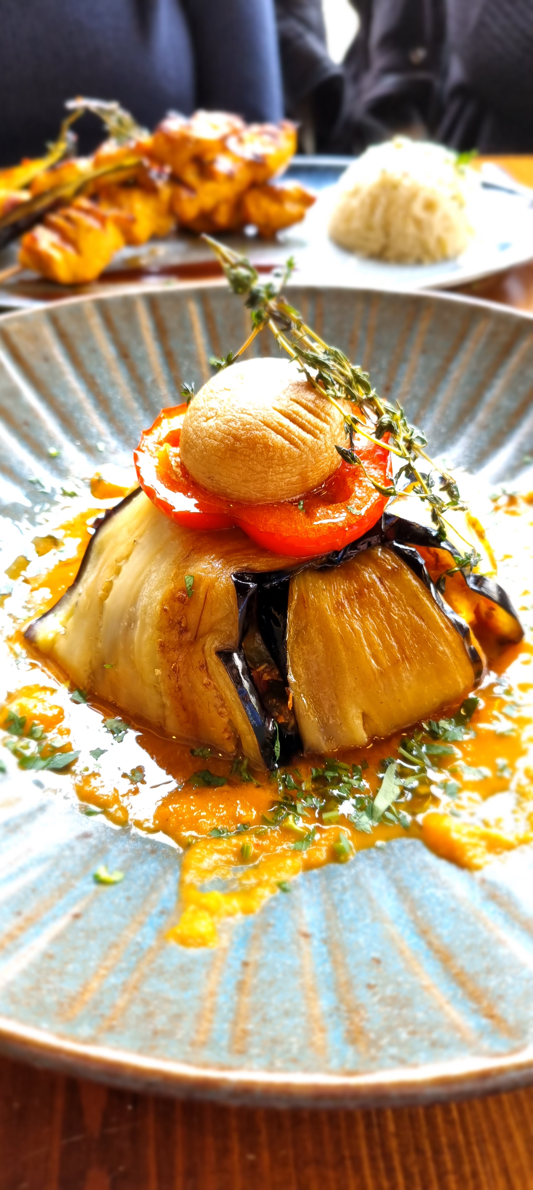 A close-up, low-angle shot of a dome-shaped dish of Rooster's Kebap, made with meat wrapped in aubergine slices and topped with a tomato and mushroom.