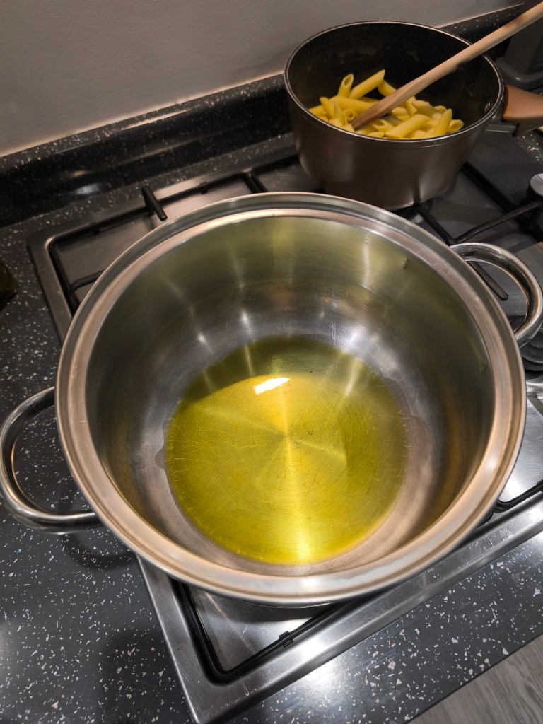 A stainless steel pot with a small pool of olive oil on the bottom, placed on a black stovetop.