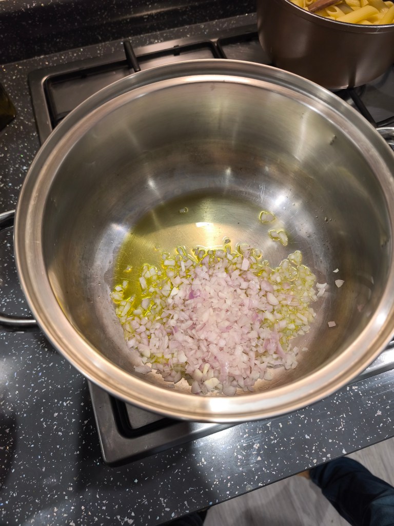 Diced shallots being sautéed in a pot with olive oil.