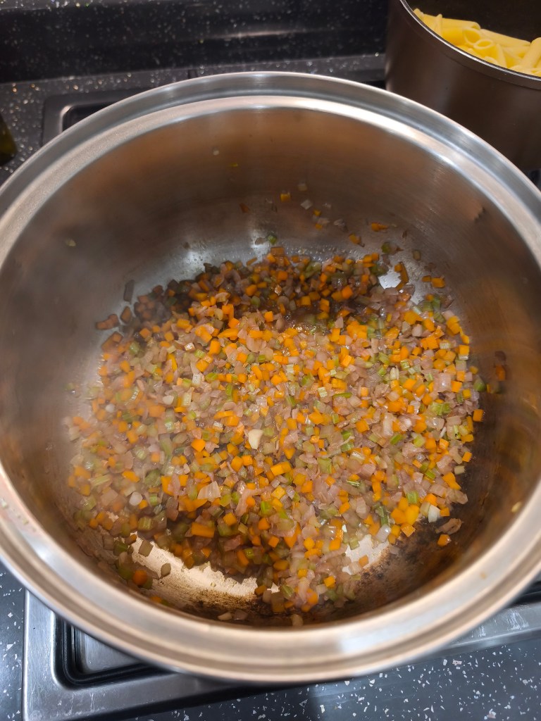 Cooked and softened diced carrots, celery, and shallots in a pot, now with a deep reddish-brown color from deglazing with red wine.