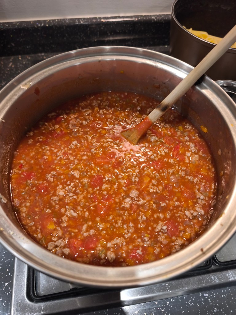 A rich red bolognese sauce simmering in a pot with a wooden spoon.