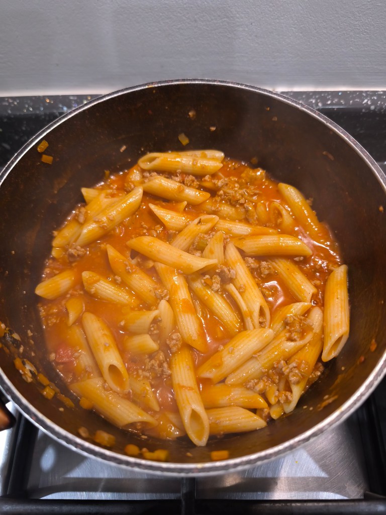 Cooked penne pasta mixed into a pot of bolognese sauce.