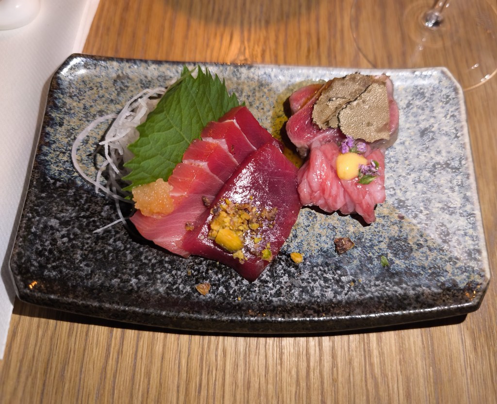 A tasting plate of various raw tuna cuts: dark red lean Akami slices with a shiso leaf, and pink fatty Kamatoro and Otoro cuts topped with truffle shavings.