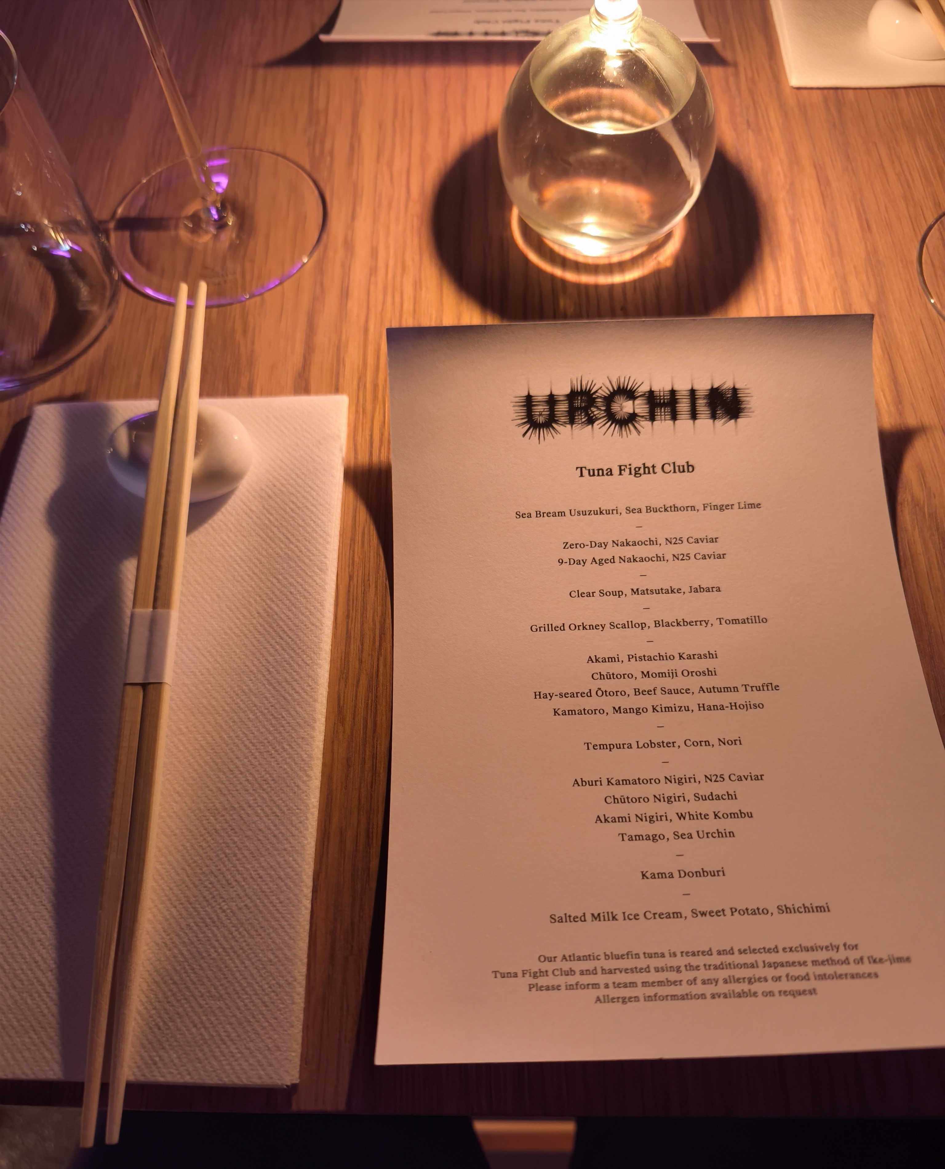 A photo of a restaurant table setting with chopsticks, a white napkin, a water glass, and the printed black-and-white menu for Urchin's Tuna Fight Club.